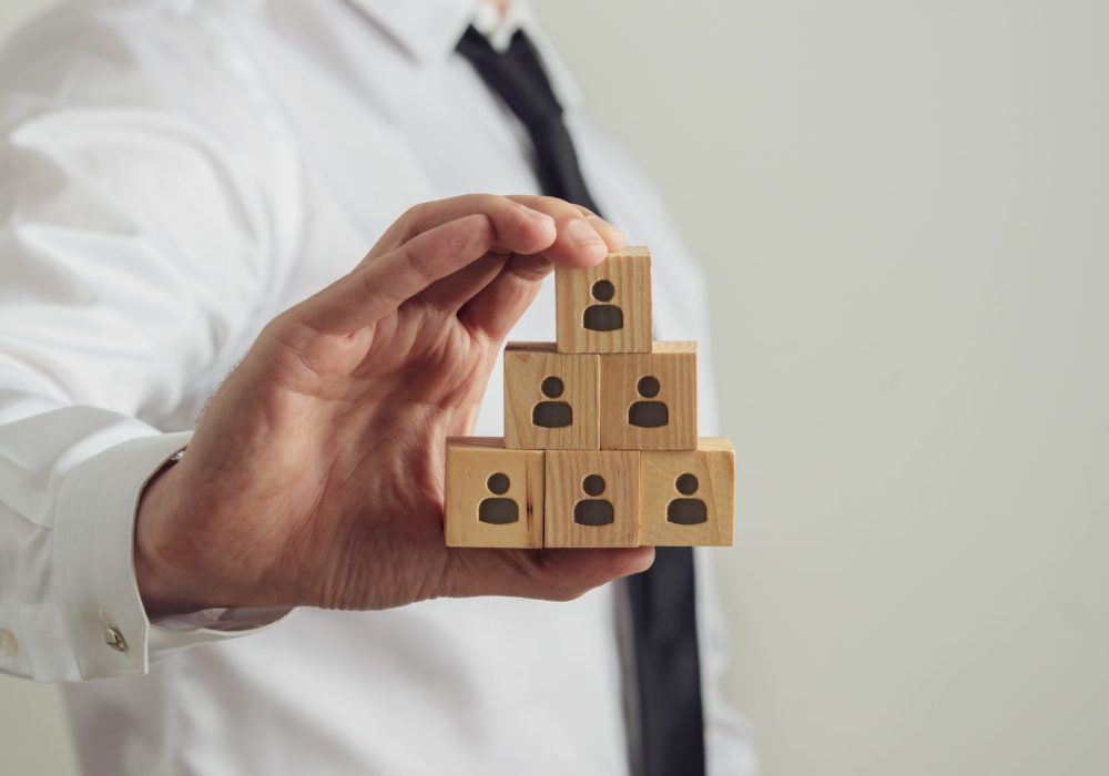 Business executive holding wooden cubes with person icon on them build in a pyramid structure. Conceptual image of employment and human resources.